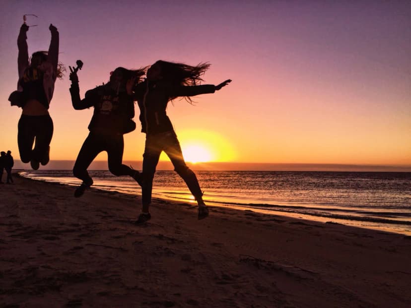 Jongeren springen op het strand bij zonsondergang tijdens een taalreis in Australië